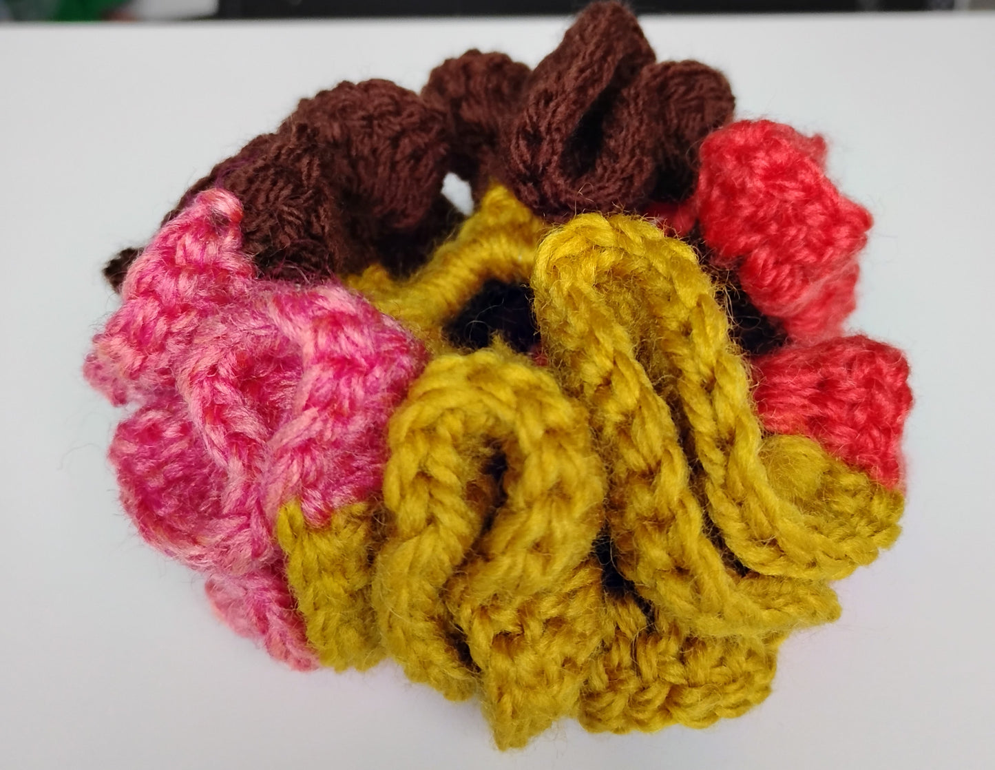 Colorful eye-catching scrunchies crochet made from vibrant yarns in pink, brown, yellow, and red.